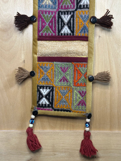 Handmade Turkish rug wall hanging with geometric designs, 3 pockets, tassels, and an evil eye charm. Upcycled vintage textile art by High Pile Designs.