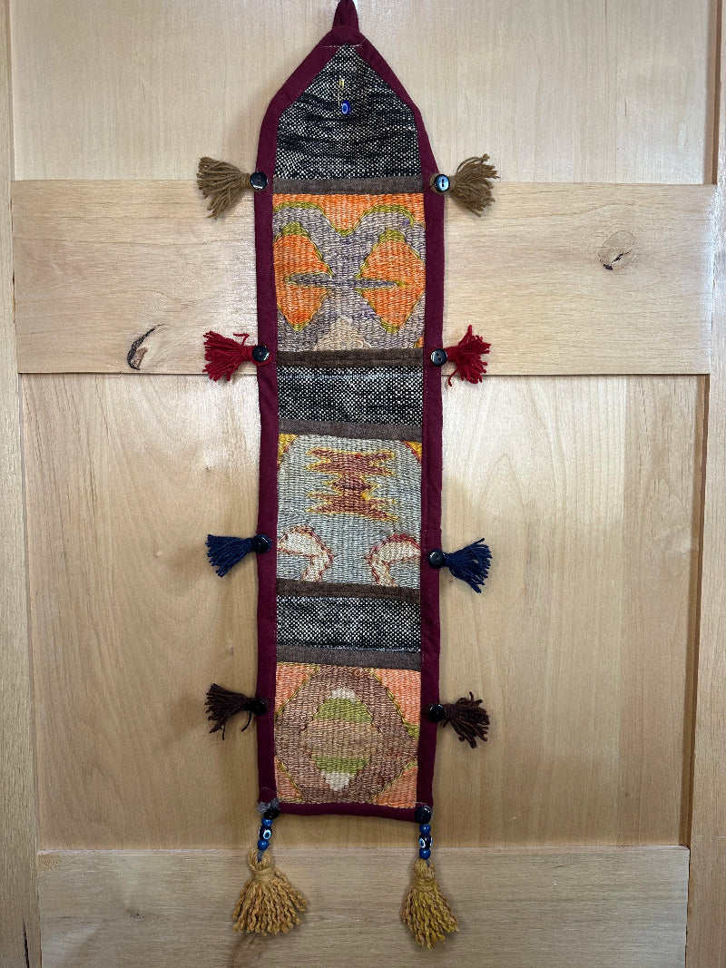 Handmade Turkish rug wall hanging with multicolor geometric designs, 3 pockets, tassels, and an evil eye charm. Upcycled vintage textile art by High Pile Designs.