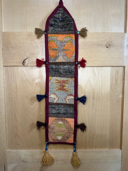 Handmade Turkish rug wall hanging with multicolor geometric designs, 3 pockets, tassels, and an evil eye charm. Upcycled vintage textile art by High Pile Designs.
