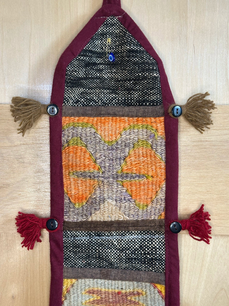 Handmade Turkish rug wall hanging with multicolor geometric designs, 3 pockets, tassels, and an evil eye charm. Upcycled vintage textile art by High Pile Designs.