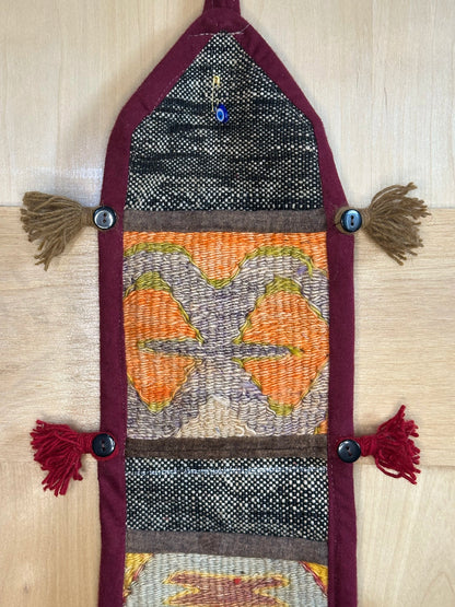 Handmade Turkish rug wall hanging with multicolor geometric designs, 3 pockets, tassels, and an evil eye charm. Upcycled vintage textile art by High Pile Designs.