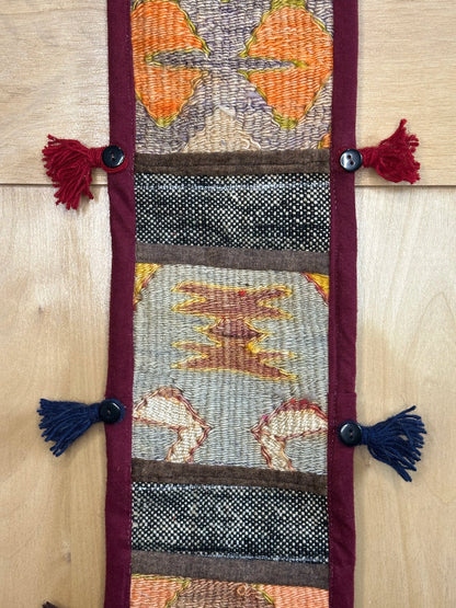 Handmade Turkish rug wall hanging with multicolor geometric designs, 3 pockets, tassels, and an evil eye charm. Upcycled vintage textile art by High Pile Designs.