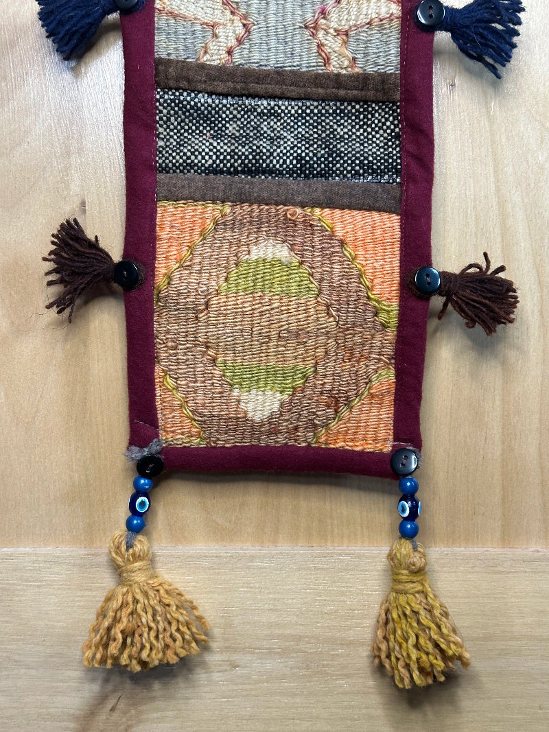 Handmade Turkish rug wall hanging with multicolor geometric designs, 3 pockets, tassels, and an evil eye charm. Upcycled vintage textile art by High Pile Designs.