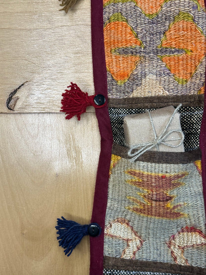 Handmade Turkish rug wall hanging with multicolor geometric designs, 3 pockets, tassels, and an evil eye charm. Upcycled vintage textile art by High Pile Designs. Featured with wrapped gift.