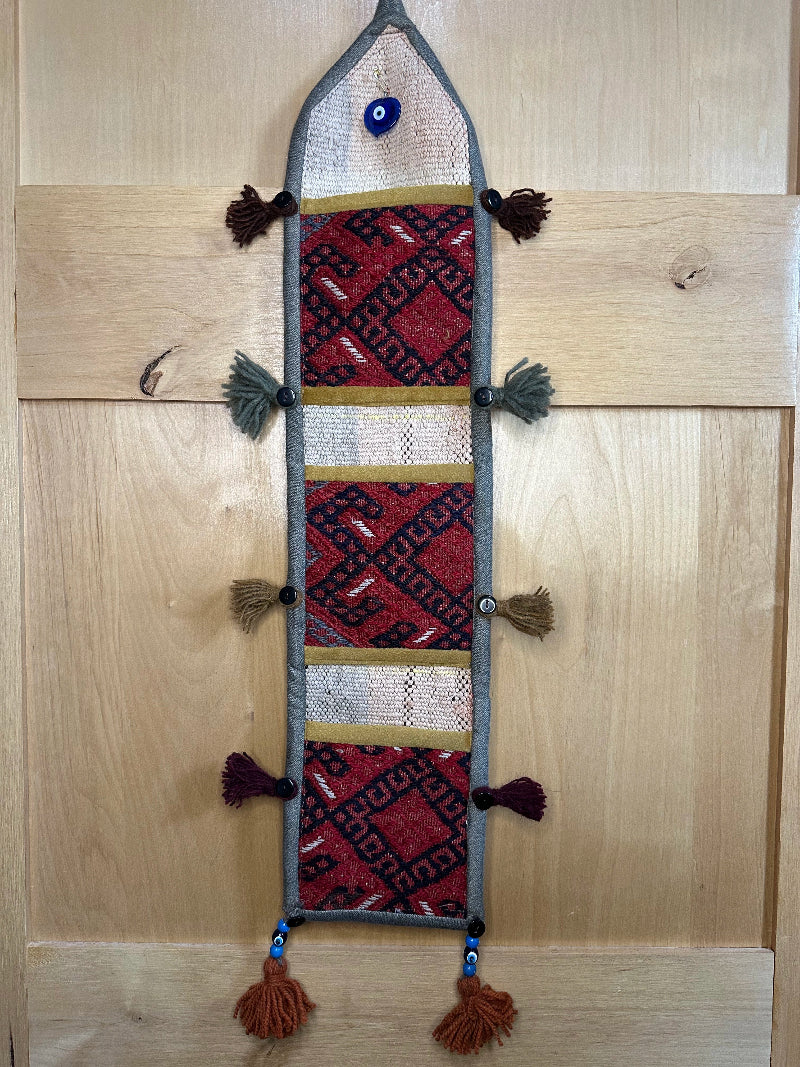 Handmade Turkish rug wall hanging with geometric designs, 3 pockets, tassels, and an evil eye charm. Upcycled vintage textile art by High Pile Designs.