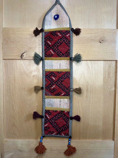 Handmade Turkish rug wall hanging with geometric designs, 3 pockets, tassels, and an evil eye charm. Upcycled vintage textile art by High Pile Designs.