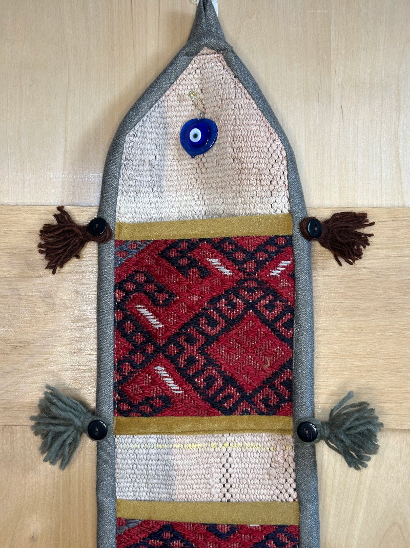 Handmade Turkish rug wall hanging with geometric designs, tassels, and an evil eye charm. Upcycled vintage textile art by High Pile Designs.