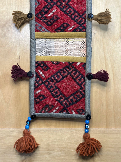 Handmade Turkish rug wall hanging with geometric designs, 3 pockets, tassels, and an evil eye charm. Upcycled vintage textile art by High Pile Designs.