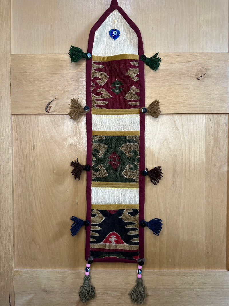 Handmade Turkish rug wall hanging with geometric designs, tassels, and an evil eye charm. Upcycled vintage textile art by High Pile Designs.
