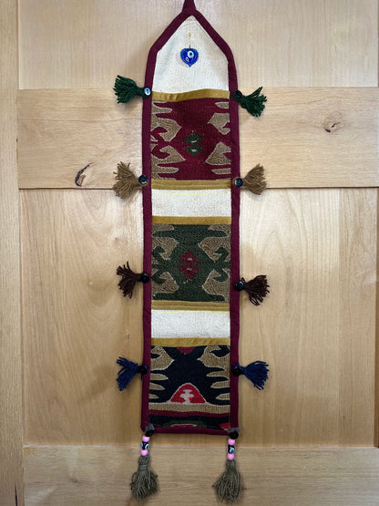 Handmade Turkish rug wall hanging with geometric designs, tassels, and an evil eye charm. Upcycled vintage textile art by High Pile Designs.