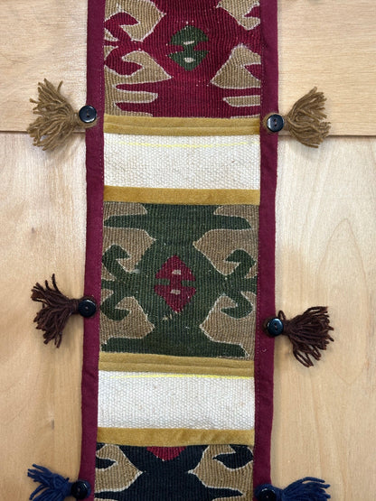 Handmade Turkish rug wall hanging with geometric designs, tassels, and an evil eye charm. Upcycled vintage textile art by High Pile Designs.