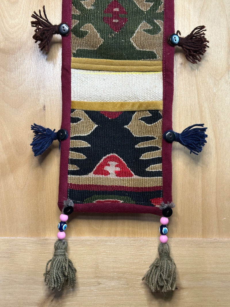 Handmade Turkish rug wall hanging with geometric designs, tassels, and an evil eye charm. Upcycled vintage textile art by High Pile Designs.