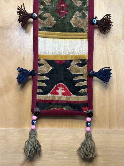 Handmade Turkish rug wall hanging with geometric designs, tassels, and an evil eye charm. Upcycled vintage textile art by High Pile Designs.
