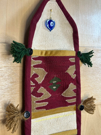Handmade Turkish rug wall hanging with geometric designs, tassels, and an evil eye charm. Upcycled vintage textile art by High Pile Designs.