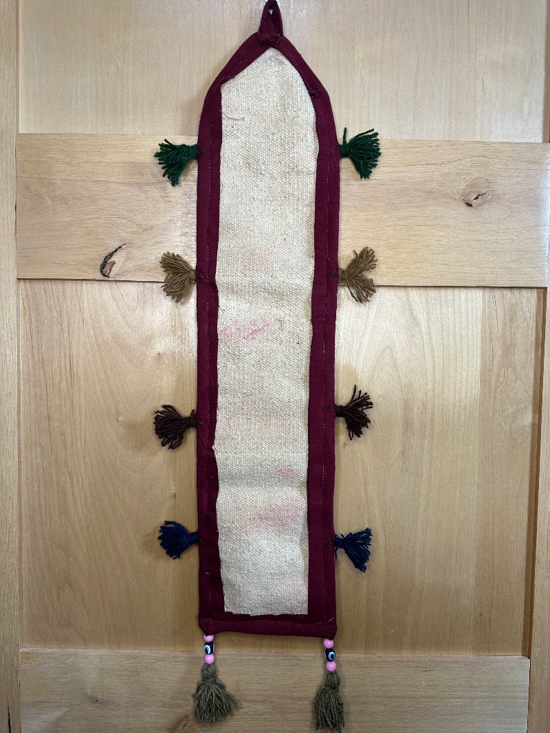 Handmade Turkish rug wall hanging with geometric designs, tassels, and an evil eye charm. Upcycled vintage textile art by High Pile Designs.