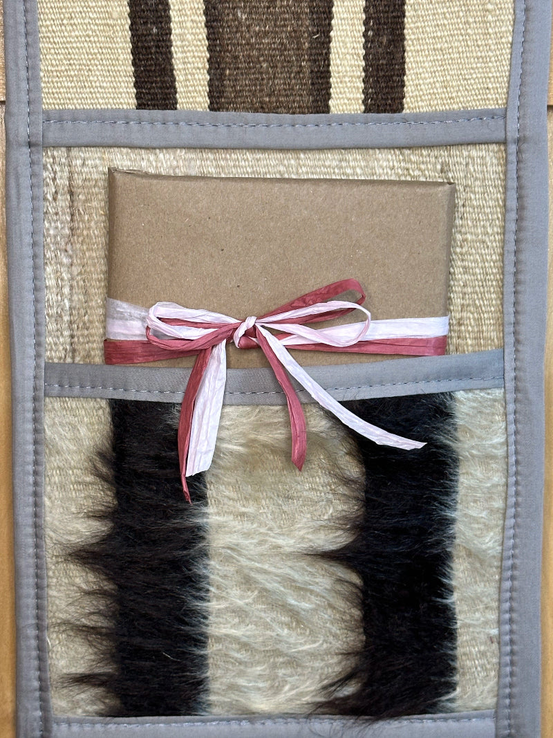 Decorative, handmade Turkish rug wall organizer with neutral stripe designs and 3 storage pockets. Upcycled vintage textile art by High Pile Designs. Featuring a wrapped gift.