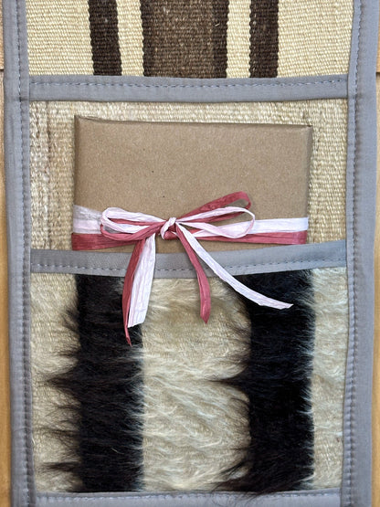 Decorative, handmade Turkish rug wall organizer with neutral stripe designs and 3 storage pockets. Upcycled vintage textile art by High Pile Designs. Featuring a wrapped gift.