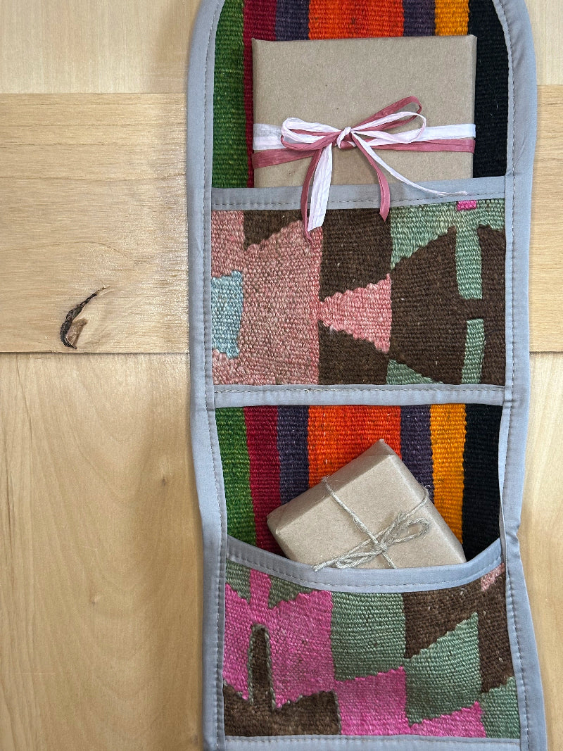 Decorative, handmade Turkish rug wall organizer with vibrant stripe designs and 3 storage pockets. Upcycled vintage textile art by High Pile Designs. Featuring wrapped gifts.