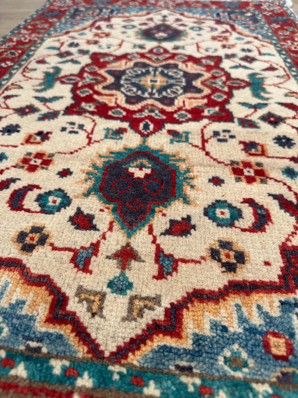 Handknotted two by three foot mini Kazak rug with intricate geometric patterns, rich red and deep blue hues, and a durable low-pile wool construction. Made to order in custom sizes, perfect for adding a bold, traditional touch to vintage, classic, or eclectic home décor.