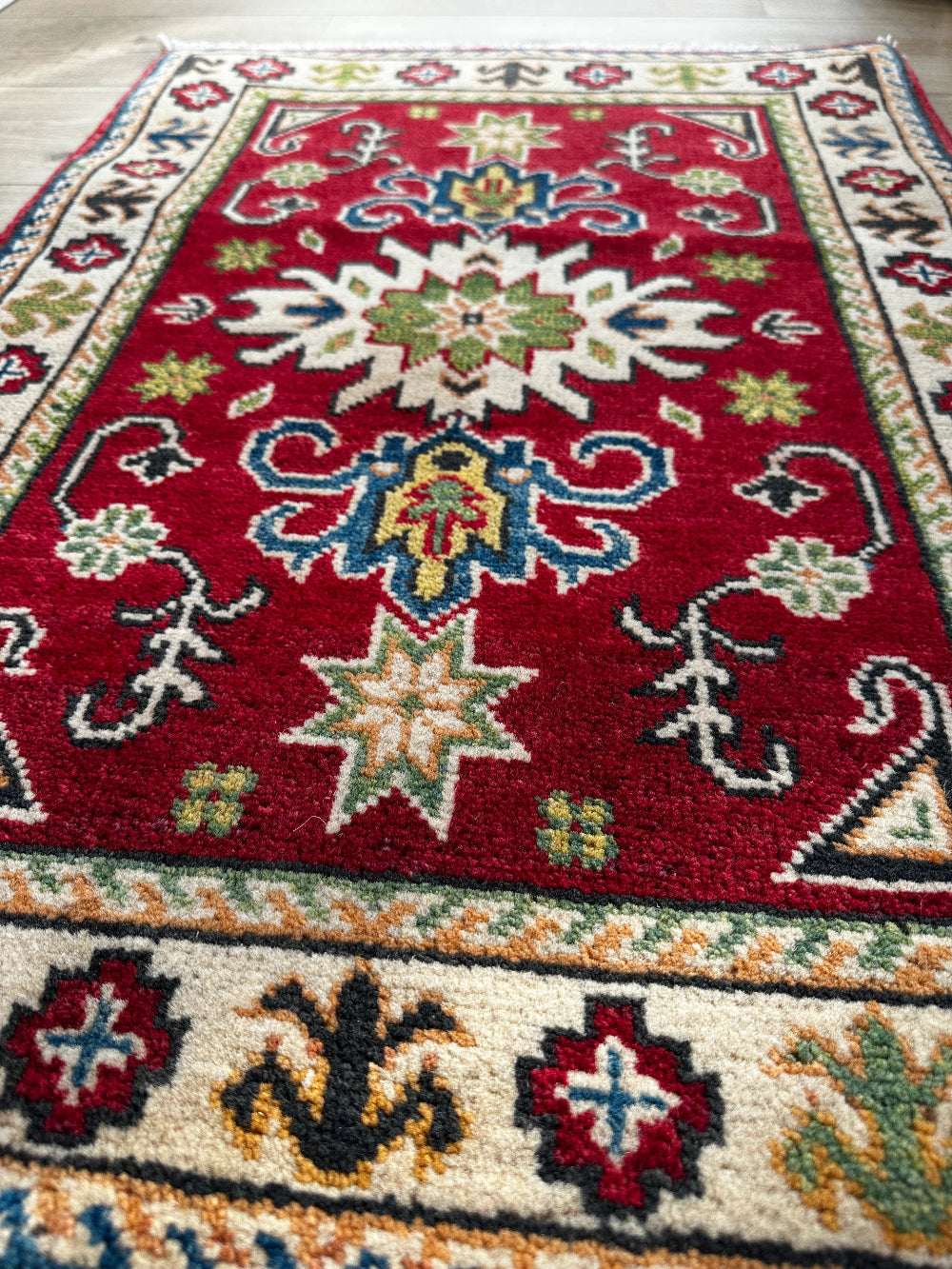 Hand-knotted 2x3 foot mini pile rug featuring a colorful geometric design, large central motif and geometric border - wool material with pops of red, green, navy and white. 