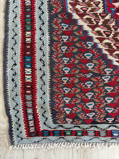 Handwoven Senneh Kilim rug, featuring intricate geometric patterns, a central medallion design, and rich earthy red, deep blue, and neutral tones. Flat-woven wool rug with fine detailing and a slit tapestry weave, perfect for bohemian, modern, or traditional home décor.