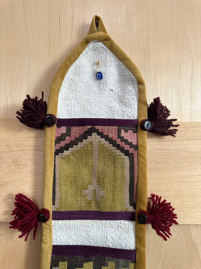 Handmade Turkish wall hanging with vintage rug patterns, featuring colorful tassels, evil eye beads, and geometric designs on a wood panel background. Unique bohemian decor made from authentic Turkish rug fragments, perfect for home styling.