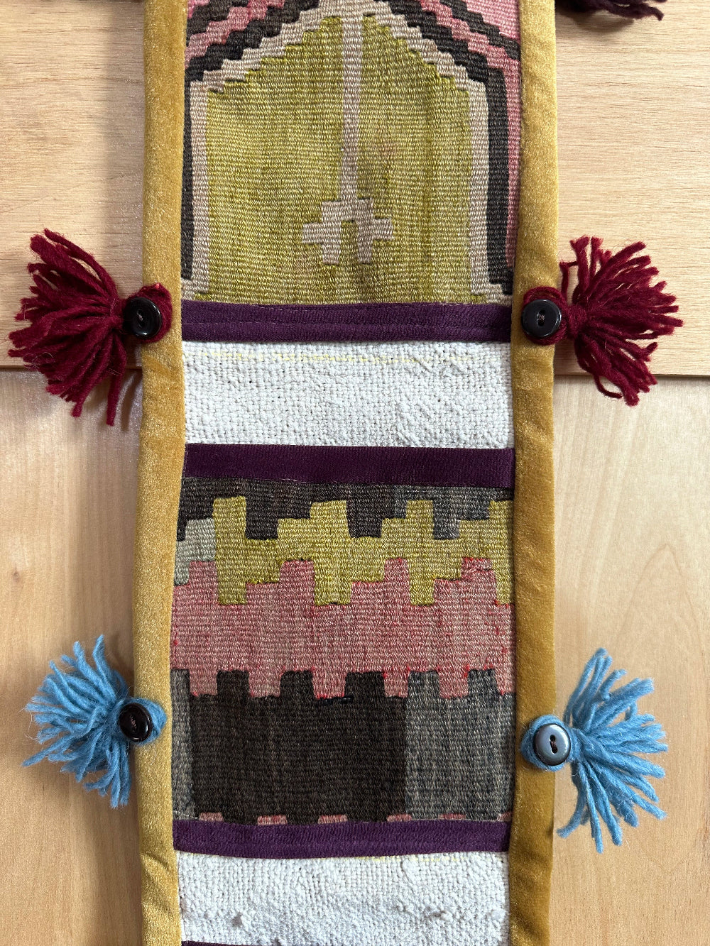 Handmade Turkish wall hanging with vintage rug patterns, featuring colorful tassels, evil eye beads, and geometric designs on a wood panel background. Unique bohemian decor made from authentic Turkish rug fragments, perfect for home styling.