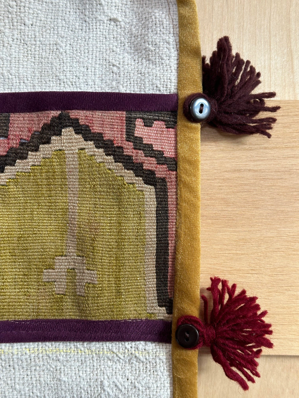 Handmade Turkish wall hanging with vintage rug patterns, featuring colorful tassels, evil eye beads, and geometric designs on a wood panel background. Unique bohemian decor made from authentic Turkish rug fragments, perfect for home styling.