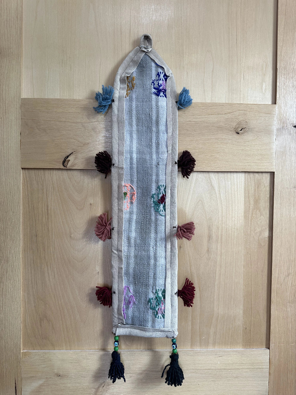 Handmade Turkish wall hanging with vintage rug patterns, featuring colorful tassels, evil eye beads, and geometric designs on a wood panel background. Unique bohemian decor made from authentic Turkish rug fragments, perfect for home styling.