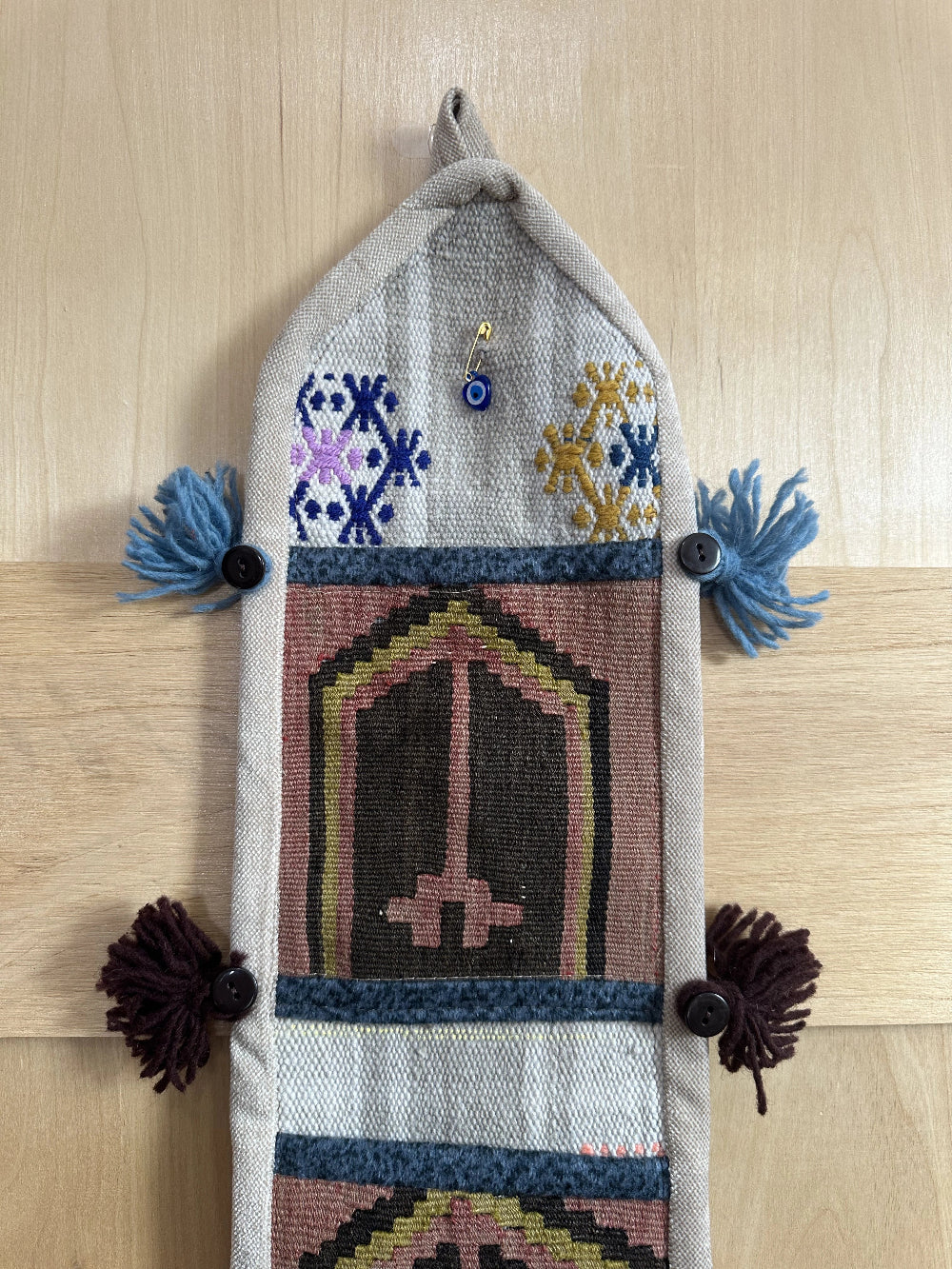 Handmade Turkish wall hanging with vintage rug patterns, featuring colorful tassels, evil eye beads, and geometric designs on a wood panel background. Unique bohemian decor made from authentic Turkish rug fragments, perfect for home styling.