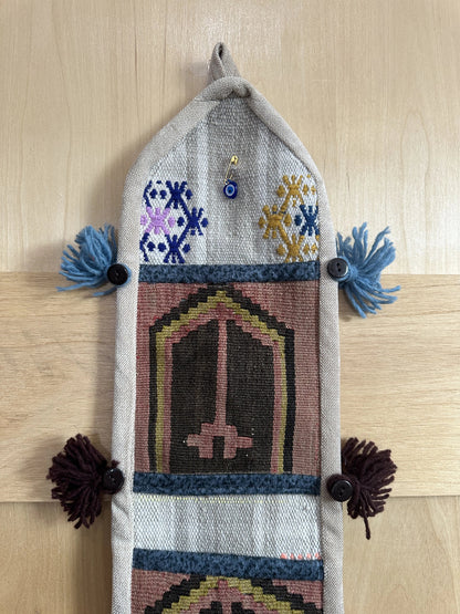 Handmade Turkish wall hanging with vintage rug patterns, featuring colorful tassels, evil eye beads, and geometric designs on a wood panel background. Unique bohemian decor made from authentic Turkish rug fragments, perfect for home styling.