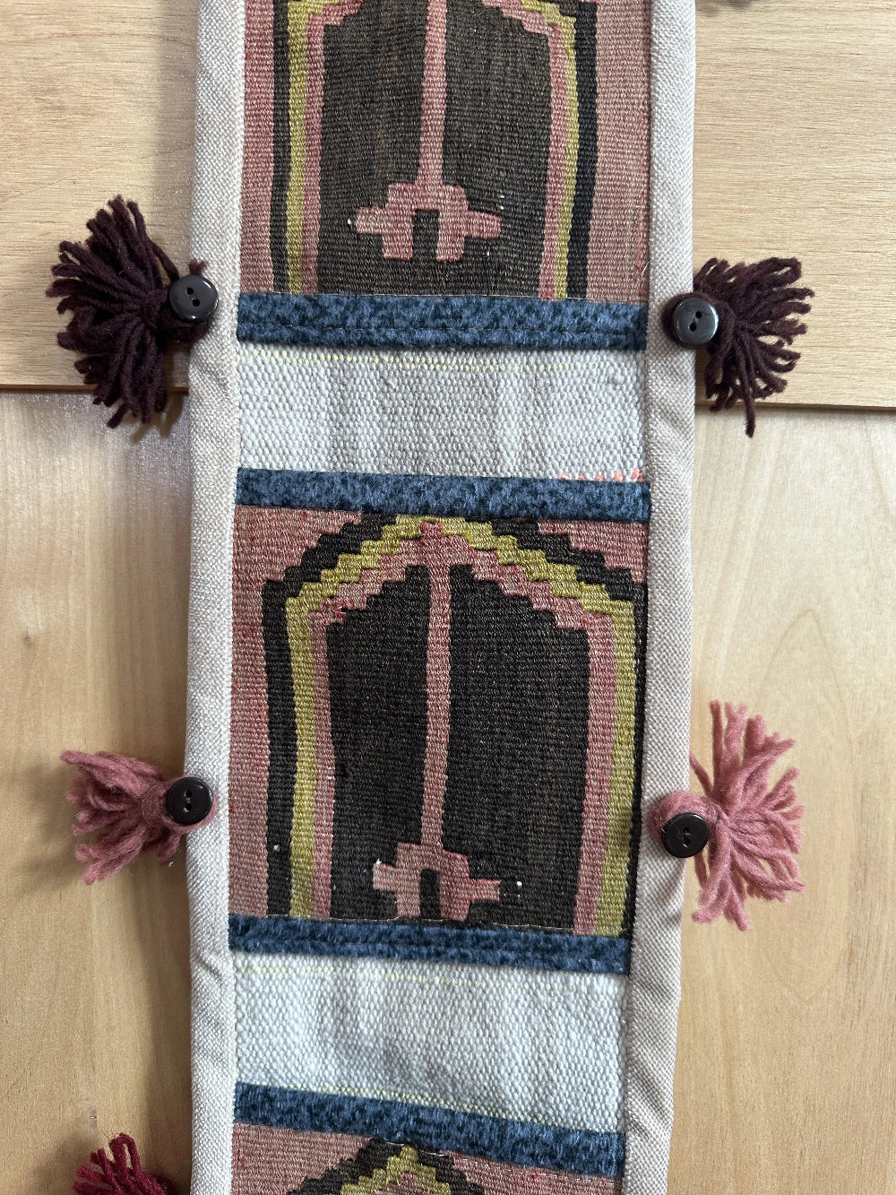 Handmade Turkish wall hanging with vintage rug patterns, featuring colorful tassels, evil eye beads, and geometric designs on a wood panel background. Unique bohemian decor made from authentic Turkish rug fragments, perfect for home styling.