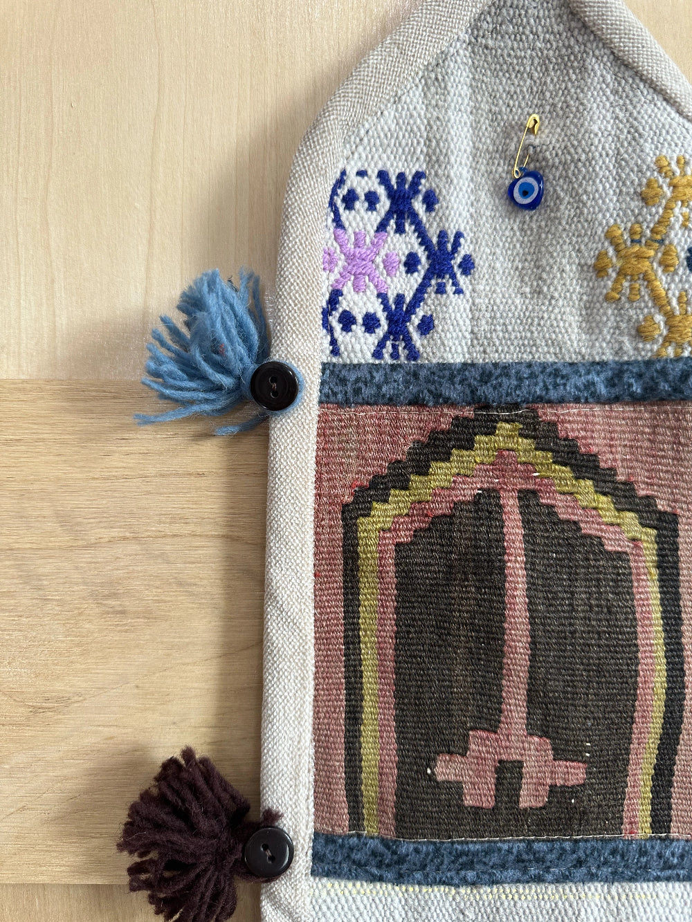 Handmade Turkish wall hanging with vintage rug patterns, featuring colorful tassels, evil eye beads, and geometric designs on a wood panel background. Unique bohemian decor made from authentic Turkish rug fragments, perfect for home styling.