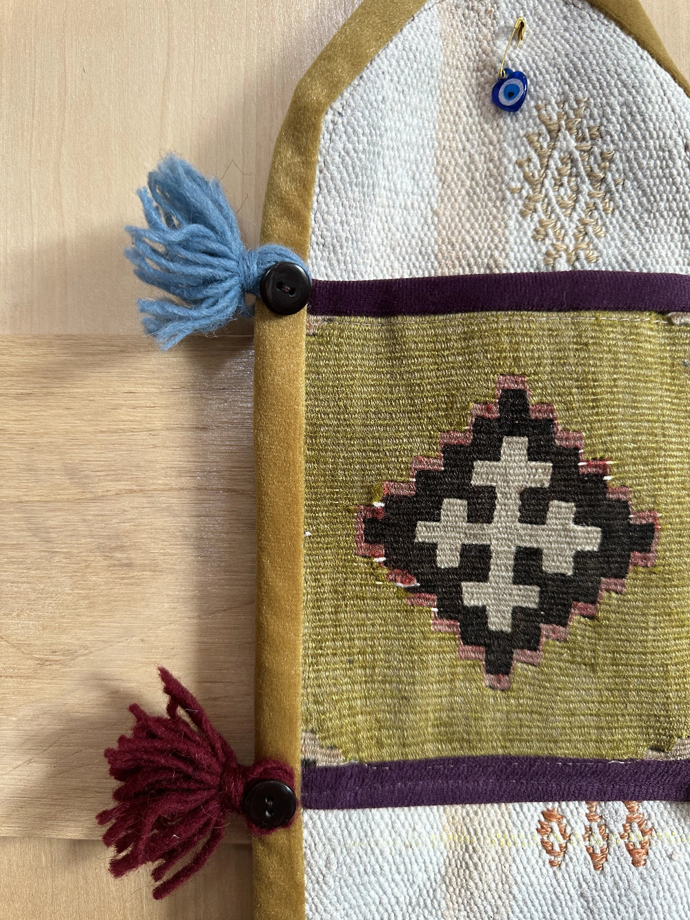 Handmade Turkish wall hanging with vintage rug patterns, featuring colorful tassels, evil eye beads, and geometric designs on a wood panel background. Unique bohemian decor made from authentic Turkish rug fragments, perfect for home styling.