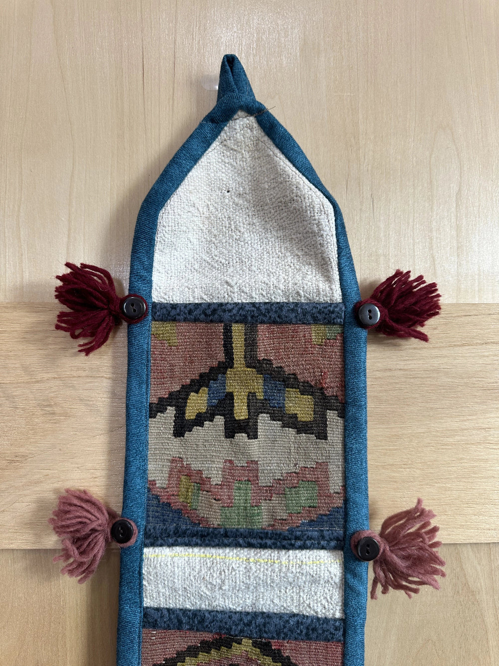 Handmade Turkish wall hanging with vintage rug patterns, featuring colorful tassels, evil eye beads, and geometric designs on a wood panel background. Unique bohemian decor made from authentic Turkish rug fragments, perfect for home styling.