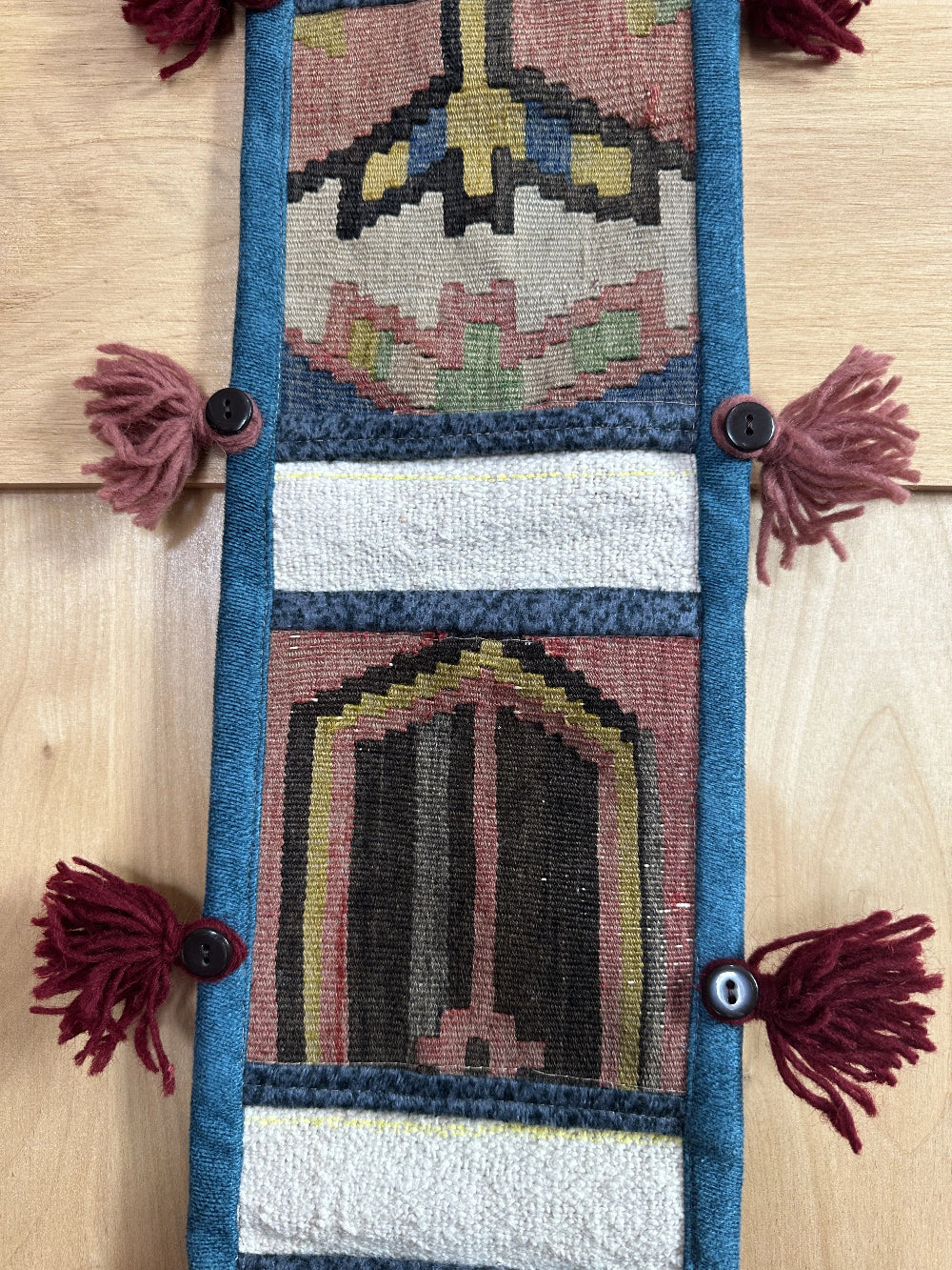 Handmade Turkish wall hanging with vintage rug patterns, featuring colorful tassels, evil eye beads, and geometric designs on a wood panel background. Unique bohemian decor made from authentic Turkish rug fragments, perfect for home styling.