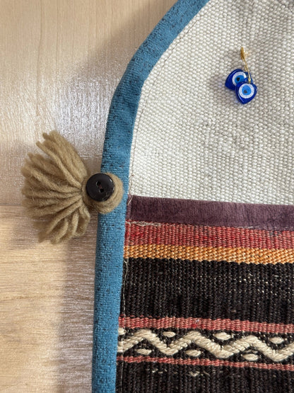 Handmade Turkish wall hanging with vintage rug patterns, featuring colorful tassels, evil eye beads, and geometric designs on a wood panel background. Unique bohemian decor made from authentic Turkish rug fragments, perfect for home styling.