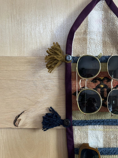 Handmade Turkish wall hanging with vintage rug patterns, featuring colorful tassels, evil eye beads, and geometric designs on a wood panel background. Unique bohemian decor made from authentic Turkish rug fragments, perfect for home styling.