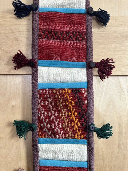 Handmade Turkish wall hanging with vintage rug patterns, featuring colorful tassels, evil eye beads, and geometric designs on a wood panel background. Unique bohemian decor made from authentic Turkish rug fragments, perfect for home styling.