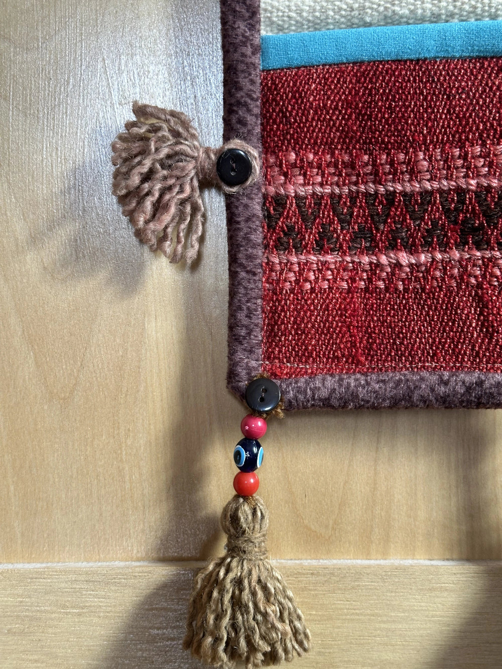 Handmade Turkish wall hanging with vintage rug patterns, featuring colorful tassels, evil eye beads, and geometric designs on a wood panel background. Unique bohemian decor made from authentic Turkish rug fragments, perfect for home styling.