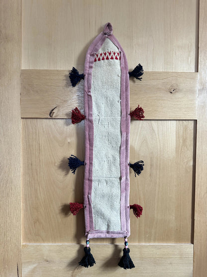 Handmade Turkish wall hanging with vintage rug patterns, featuring colorful tassels, evil eye beads, and geometric designs on a wood panel background. Unique bohemian decor made from authentic Turkish rug fragments, perfect for home styling.