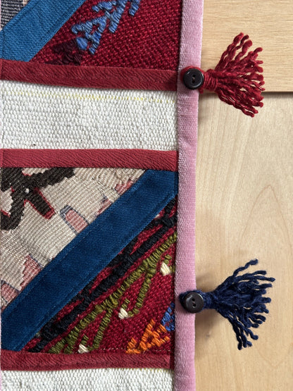 Handmade Turkish wall hanging with vintage rug patterns, featuring colorful tassels, evil eye beads, and geometric designs on a wood panel background. Unique bohemian decor made from authentic Turkish rug fragments, perfect for home styling.