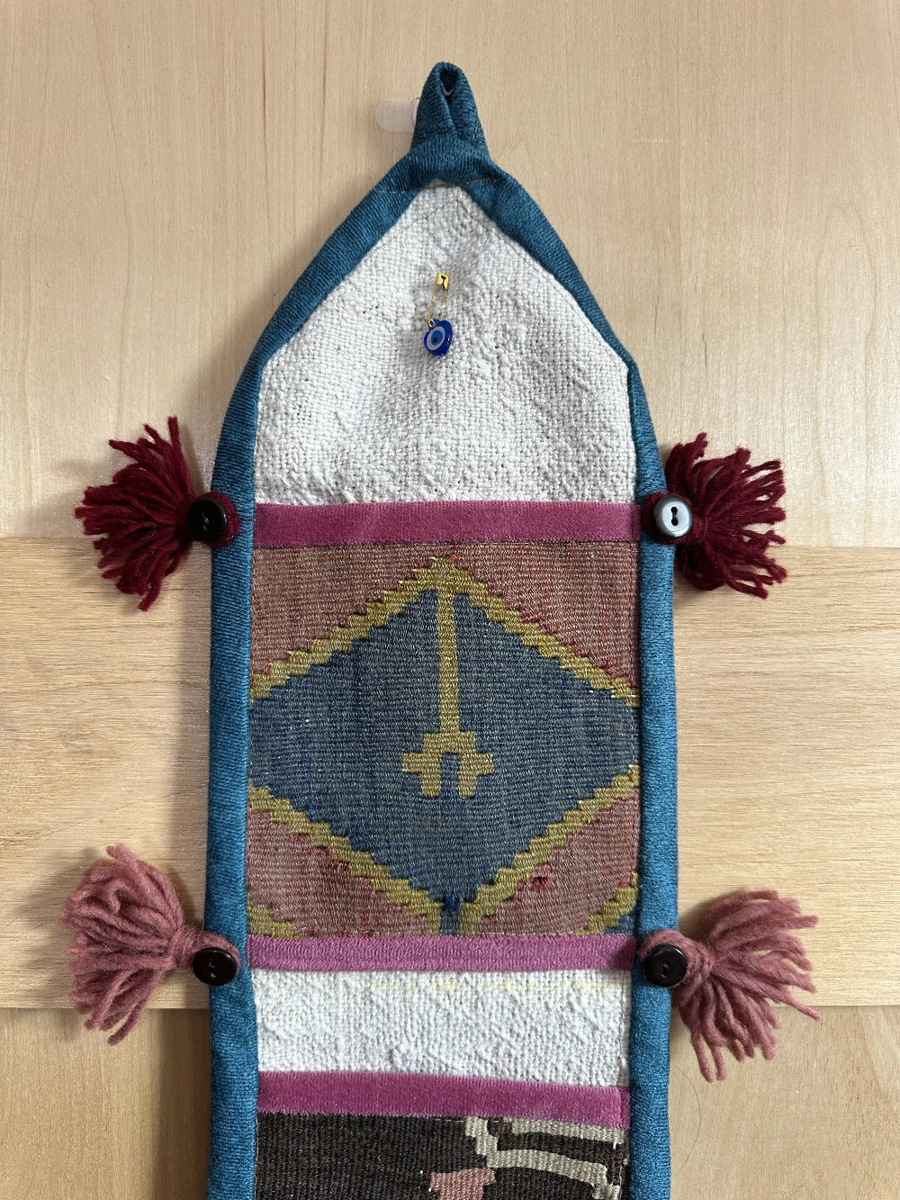 Handmade Turkish wall hanging with vintage rug patterns, featuring colorful tassels, evil eye beads, and geometric designs on a wood panel background. Unique bohemian decor made from authentic Turkish rug fragments, perfect for home styling.