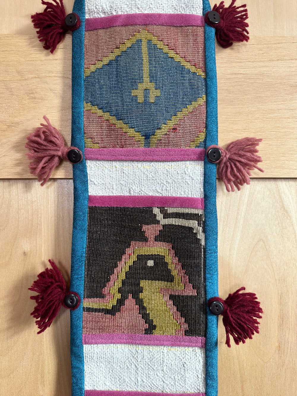 Handmade Turkish wall hanging with vintage rug patterns, featuring colorful tassels, evil eye beads, and geometric designs on a wood panel background. Unique bohemian decor made from authentic Turkish rug fragments, perfect for home styling.