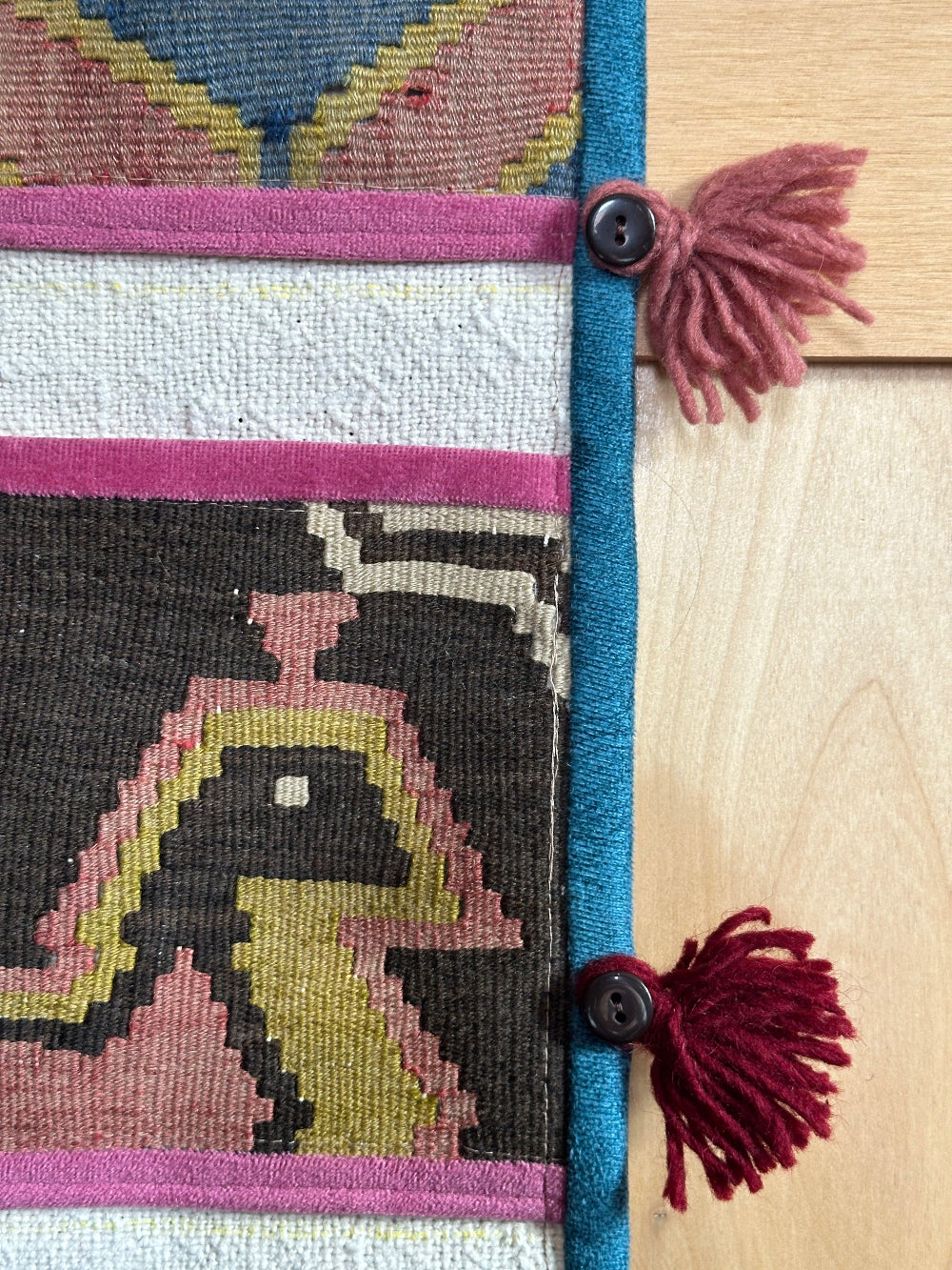 Handmade Turkish wall hanging with vintage rug patterns, featuring colorful tassels, evil eye beads, and geometric designs on a wood panel background. Unique bohemian decor made from authentic Turkish rug fragments, perfect for home styling.