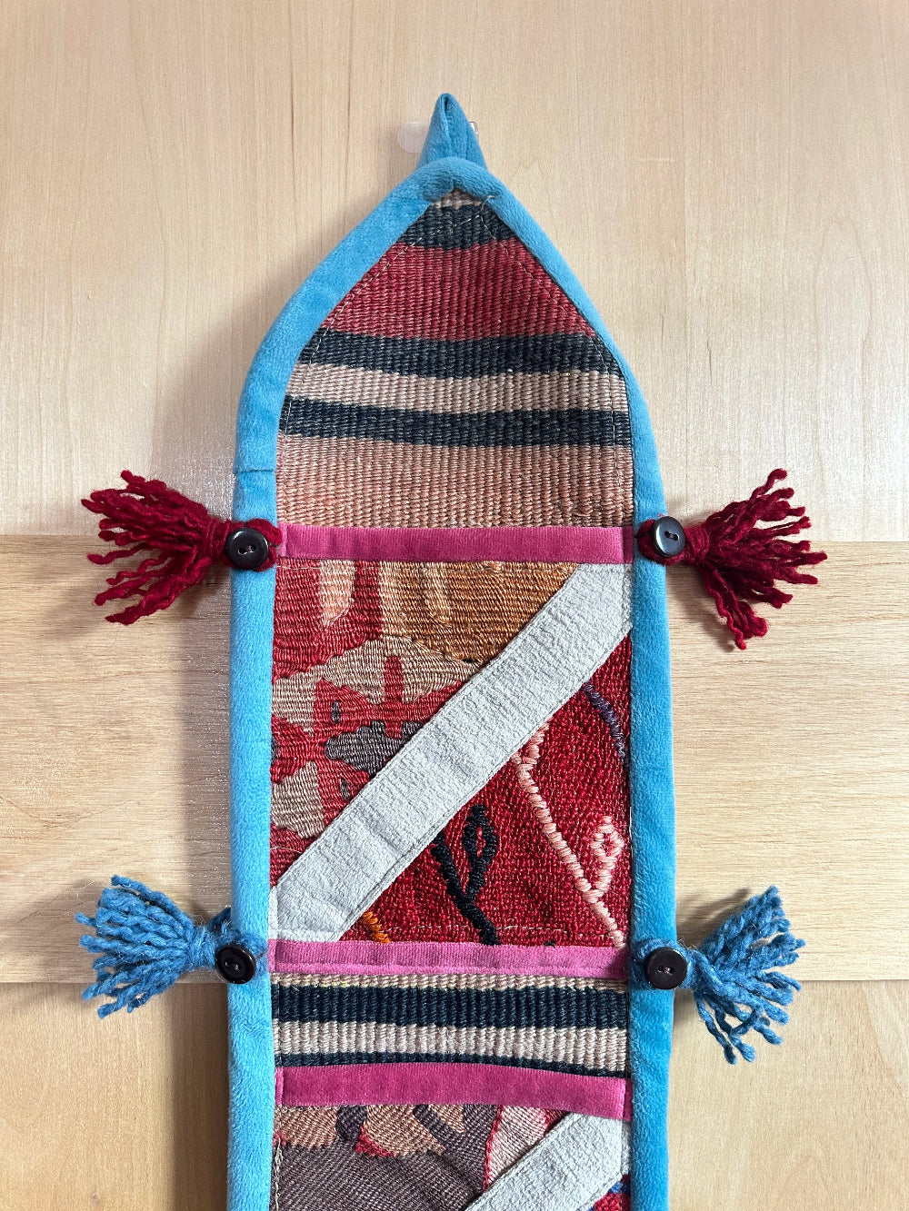 Handmade Turkish wall hanging with vintage rug patterns, featuring colorful tassels, evil eye beads, and geometric designs on a wood panel background. Unique bohemian decor made from authentic Turkish rug fragments, perfect for home styling.