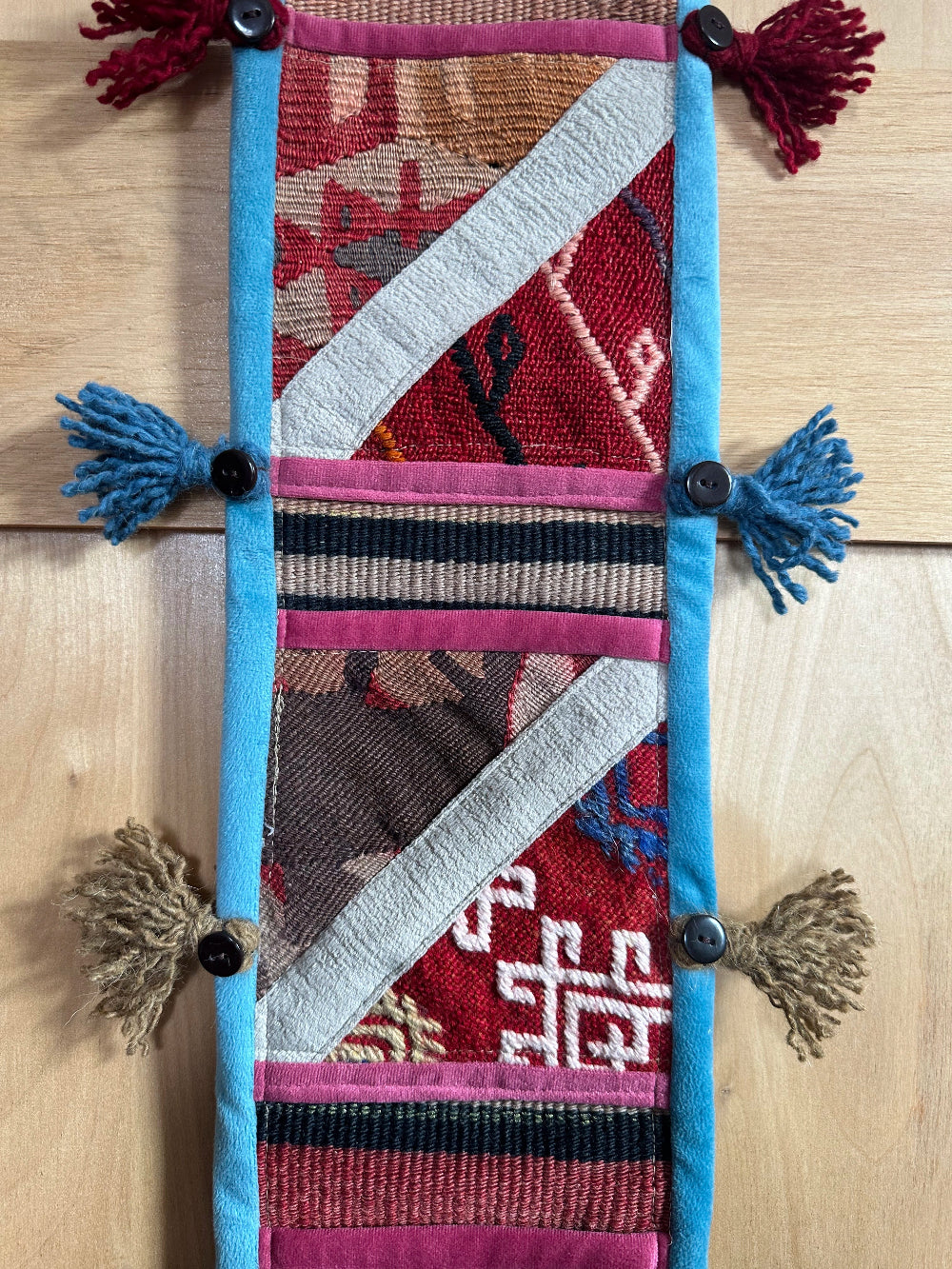 Handmade Turkish wall hanging with vintage rug patterns, featuring colorful tassels, evil eye beads, and geometric designs on a wood panel background. Unique bohemian decor made from authentic Turkish rug fragments, perfect for home styling.