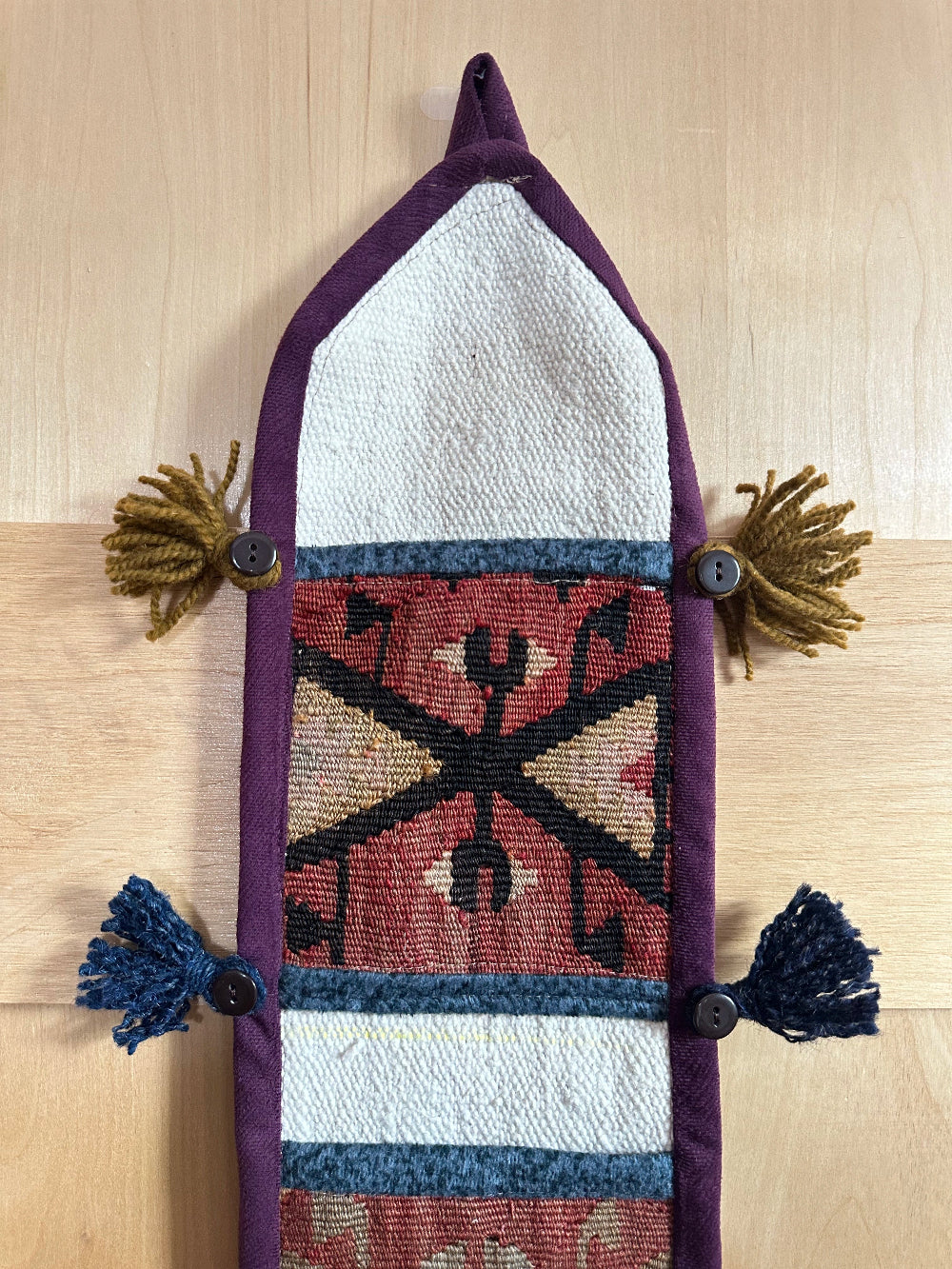 Handmade Turkish wall hanging with vintage rug patterns, featuring colorful tassels, evil eye beads, and geometric designs on a wood panel background. Unique bohemian decor made from authentic Turkish rug fragments, perfect for home styling.