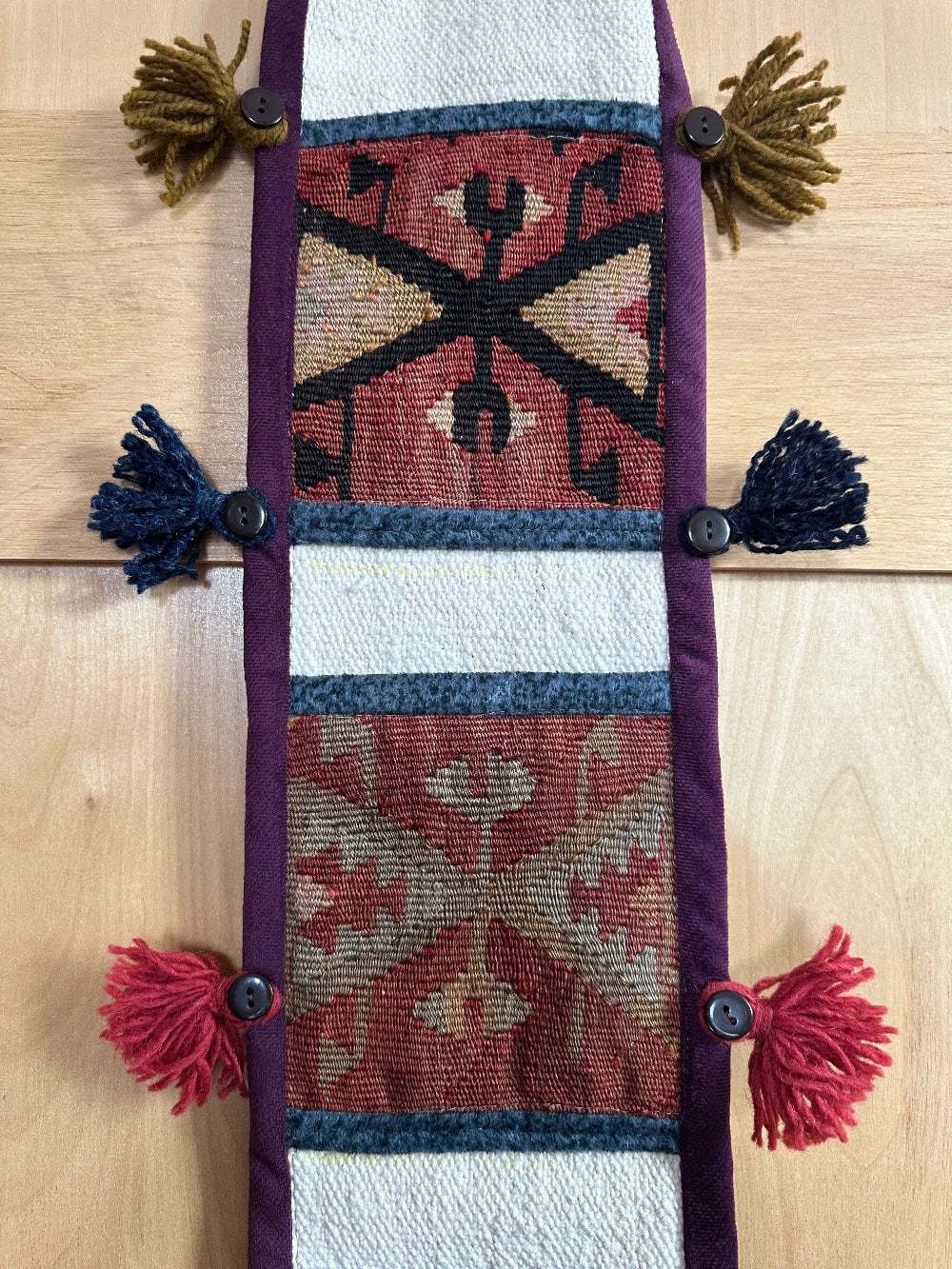 Handmade Turkish wall hanging with vintage rug patterns, featuring colorful tassels, evil eye beads, and geometric designs on a wood panel background. Unique bohemian decor made from authentic Turkish rug fragments, perfect for home styling.