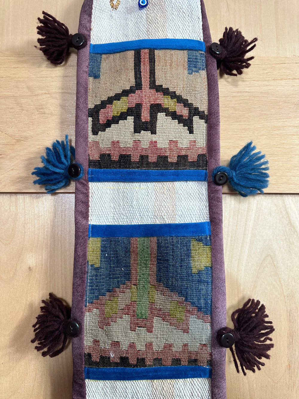 Handmade Turkish wall hanging with vintage rug patterns, featuring colorful tassels, evil eye beads, and geometric designs on a wood panel background. Unique bohemian decor made from authentic Turkish rug fragments, perfect for home styling.